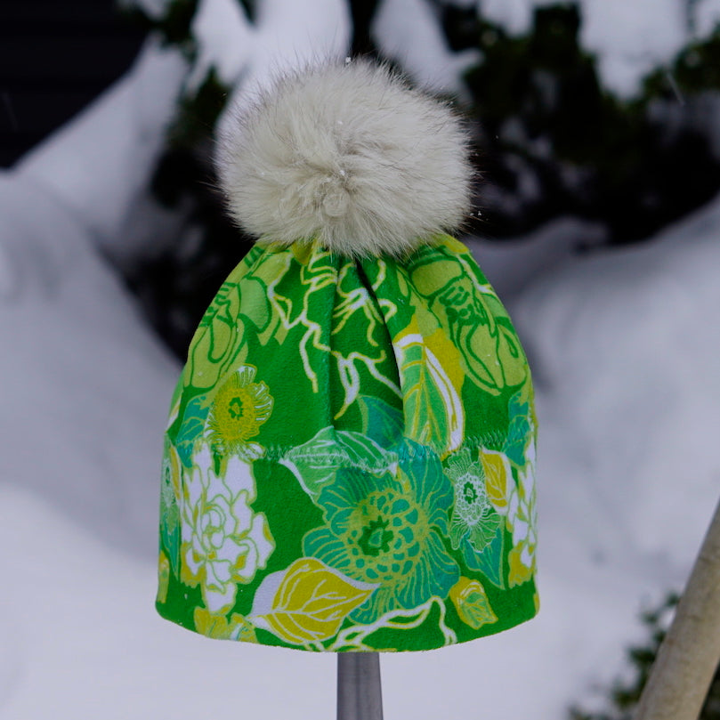 Bilde av grønn blomstrete lue med pelsdusk i snøen.